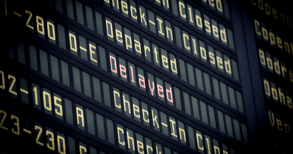 A digital board of flight numbers and status is shown, with the word 'delayed' highlighted in red